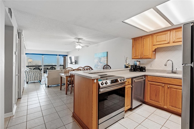 kitchen featuring tasteful backsplash, stainless steel appliances, sink, kitchen peninsula, and ceiling fan