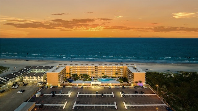 aerial view at dusk featuring a water view and a view of the beach