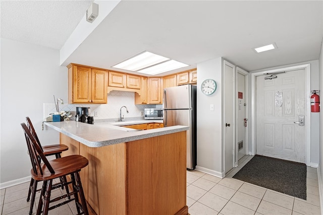 kitchen featuring kitchen peninsula, light tile patterned floors, appliances with stainless steel finishes, and tasteful backsplash