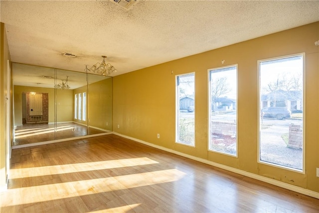 spare room with wood-type flooring, a wealth of natural light, and a chandelier