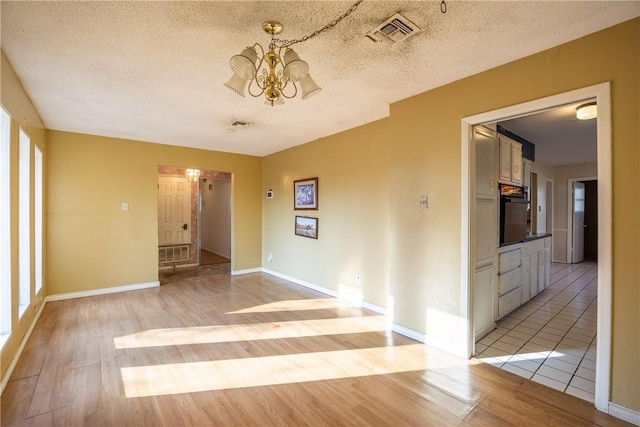 empty room with a notable chandelier, a textured ceiling, and light wood-type flooring