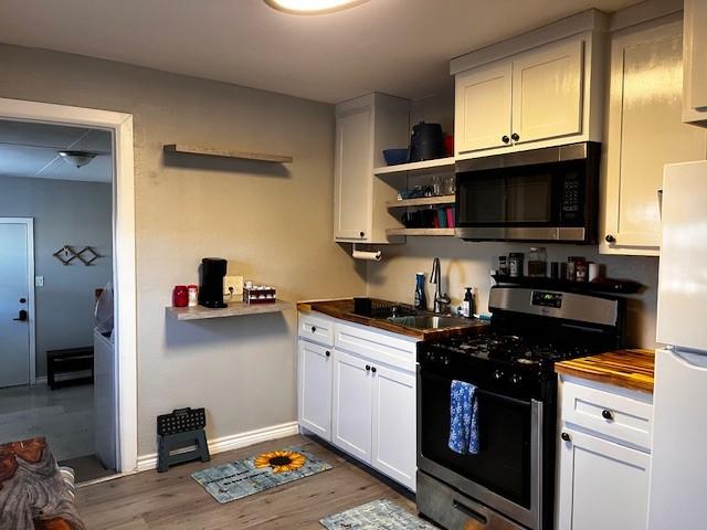 kitchen with sink, light hardwood / wood-style flooring, wooden counters, white cabinets, and appliances with stainless steel finishes