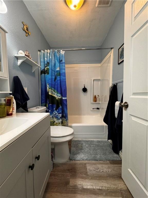 full bathroom featuring hardwood / wood-style floors, vanity, toilet, shower / bath combo with shower curtain, and a textured ceiling