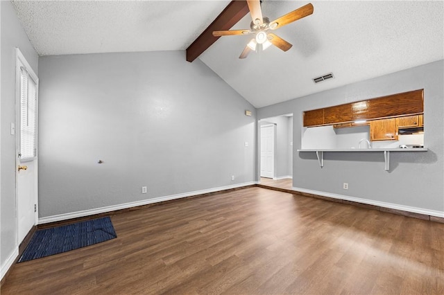 unfurnished living room featuring lofted ceiling with beams, ceiling fan, wood-type flooring, and a textured ceiling