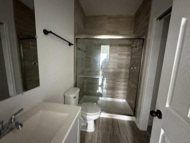 bathroom featuring vanity, wood finished floors, a shower stall, and toilet