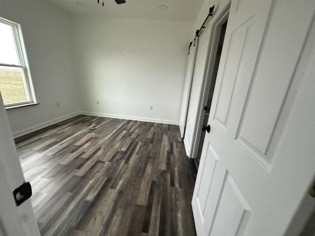 unfurnished bedroom with dark wood-style flooring, baseboards, and a barn door