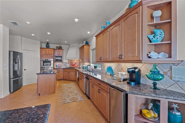 kitchen featuring stainless steel appliances, dark stone counters, premium range hood, and a center island