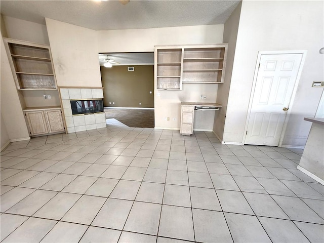 unfurnished living room with ceiling fan, light tile patterned flooring, a tile fireplace, and built in shelves