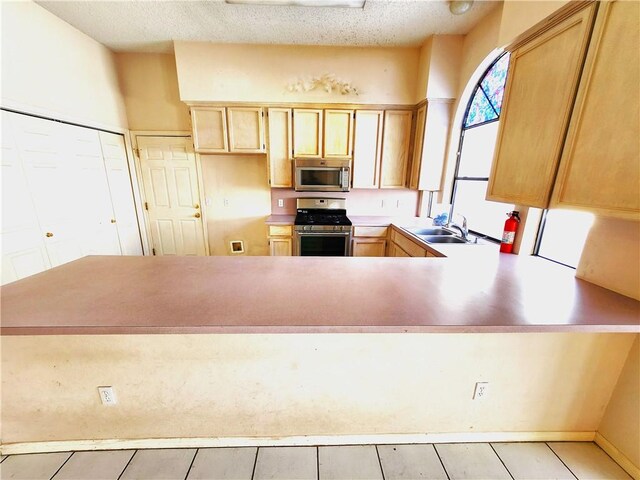 2210 Dorsey St, Corpus Christi, TX 78414 - kitchen with stainless steel appliances, a peninsula, light countertops, light brown cabinetry, and a textured ceiling