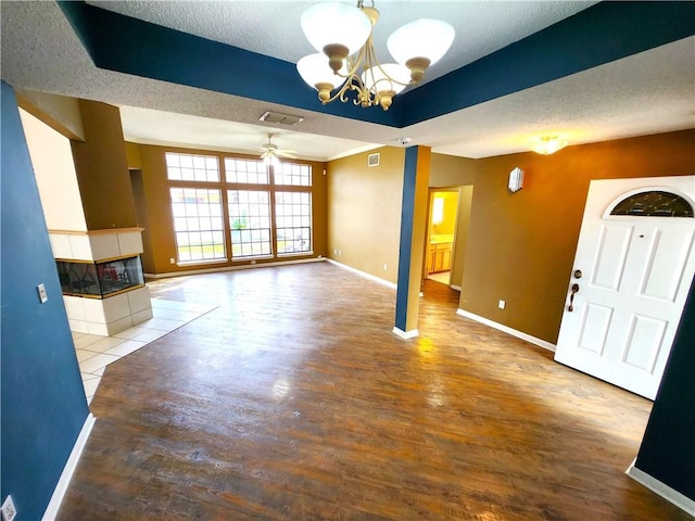 unfurnished living room with a textured ceiling, ceiling fan with notable chandelier, and hardwood / wood-style flooring