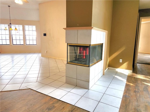 unfurnished living room with a tiled fireplace, light tile patterned floors, and a chandelier