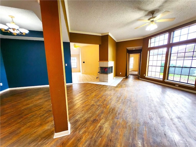 unfurnished living room featuring crown molding, hardwood / wood-style floors, a textured ceiling, a tiled fireplace, and ceiling fan with notable chandelier