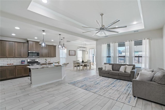 living room with a raised ceiling, ceiling fan, ornamental molding, and sink