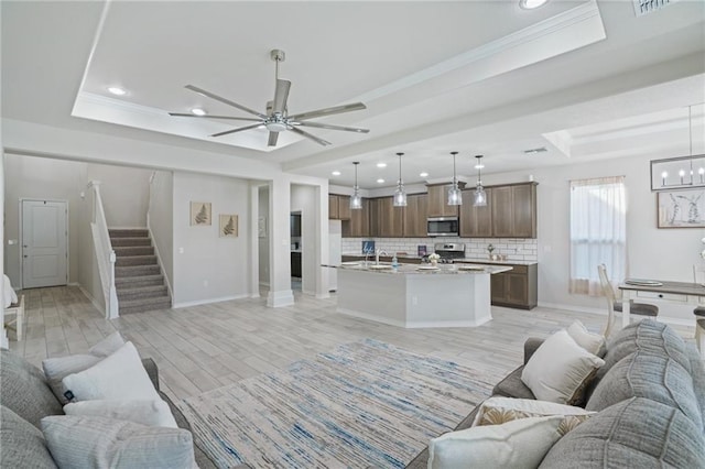 living room with a raised ceiling, sink, ceiling fan with notable chandelier, and light wood-type flooring