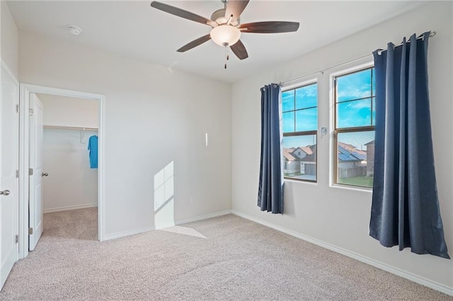 unfurnished bedroom with light carpet, a closet, a spacious closet, and ceiling fan