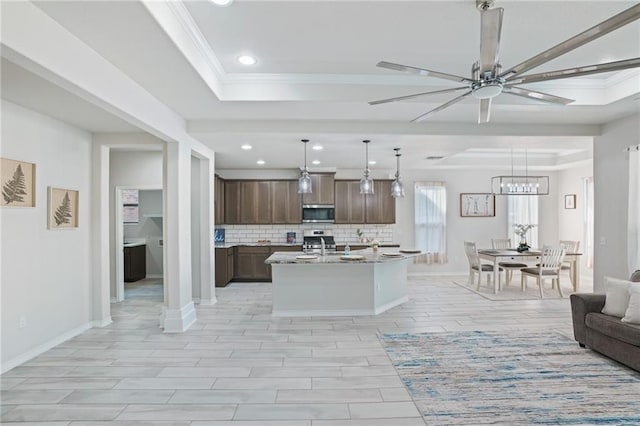 kitchen featuring a tray ceiling, hanging light fixtures, an island with sink, and stainless steel appliances