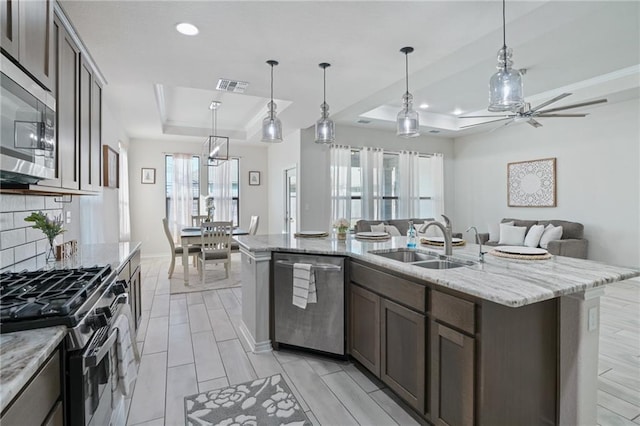 kitchen featuring hanging light fixtures, sink, an island with sink, appliances with stainless steel finishes, and a tray ceiling