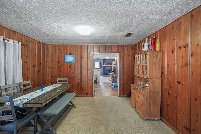 dining area with visible vents, a textured ceiling, wooden walls, a fireplace, and light colored carpet