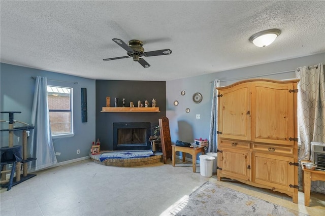 living area with a ceiling fan, a fireplace with raised hearth, baseboards, and a textured ceiling