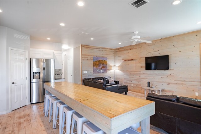 kitchen featuring light hardwood / wood-style floors, white cabinetry, a breakfast bar, stainless steel fridge with ice dispenser, and wooden walls