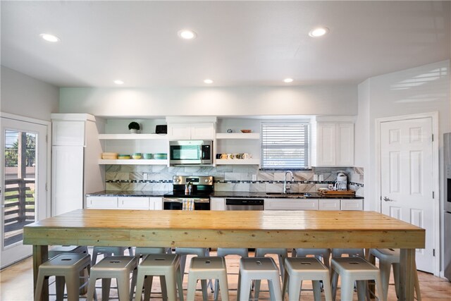 kitchen featuring stainless steel appliances, sink, a kitchen bar, white cabinets, and decorative backsplash