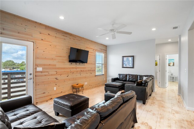 living room featuring light wood-type flooring, wooden walls, and a healthy amount of sunlight