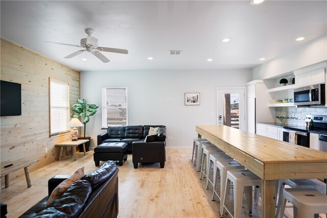 living room with light hardwood / wood-style floors, wooden walls, and ceiling fan