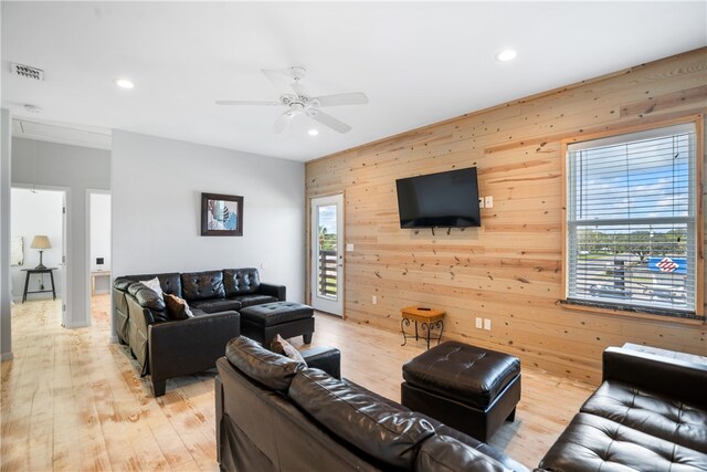 living room featuring wood walls, a wealth of natural light, ceiling fan, and light hardwood / wood-style flooring