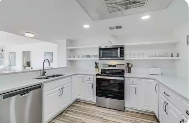 kitchen with stainless steel appliances, a sink, visible vents, open shelves, and light countertops