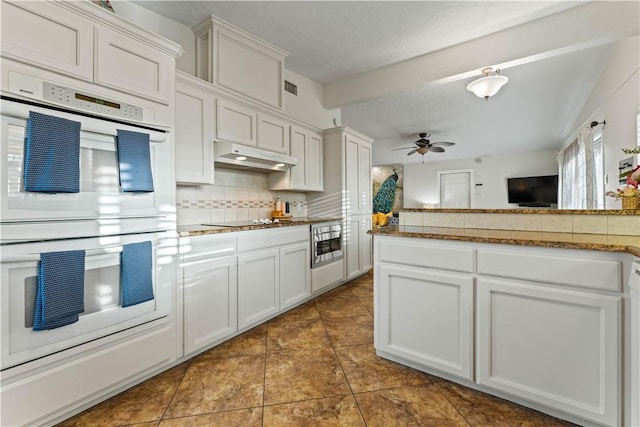 kitchen with ceiling fan, decorative backsplash, under cabinet range hood, double oven, and black electric cooktop