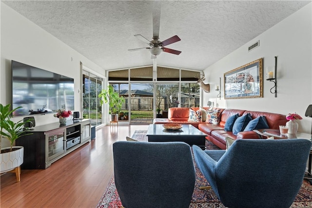 living area featuring a ceiling fan, wood finished floors, visible vents, lofted ceiling, and a textured ceiling