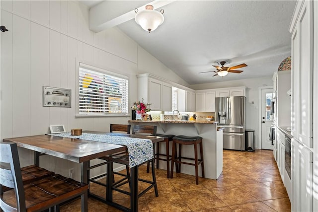 kitchen with vaulted ceiling with beams, stainless steel fridge with ice dispenser, a kitchen bar, a peninsula, and white cabinets