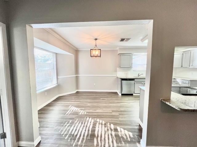 unfurnished dining area with sink, light wood-type flooring, crown molding, and an inviting chandelier