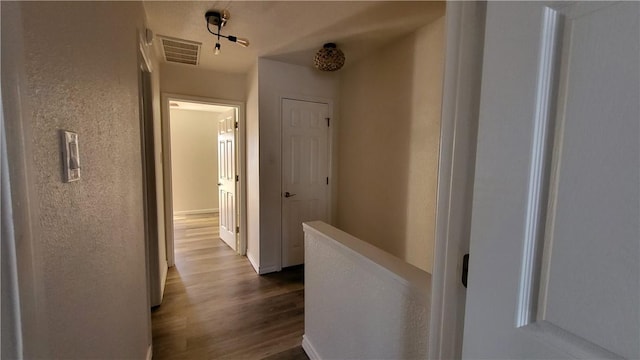 corridor featuring dark wood-style floors, visible vents, and an upstairs landing