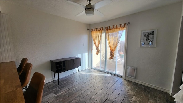 dining area with ceiling fan, a textured wall, dark wood-style flooring, and baseboards