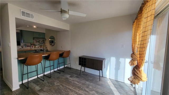 bar featuring visible vents, decorative backsplash, a ceiling fan, dark wood-type flooring, and a sink