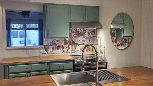 kitchen featuring butcher block countertops, green cabinetry, a sink, and under cabinet range hood