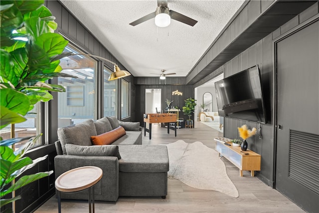 living room with wood walls, light hardwood / wood-style flooring, ceiling fan, and a textured ceiling