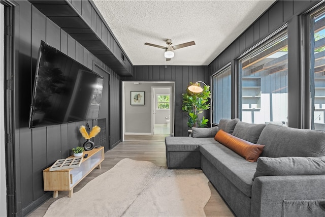 living room with a textured ceiling, light wood-type flooring, ceiling fan, and wooden walls