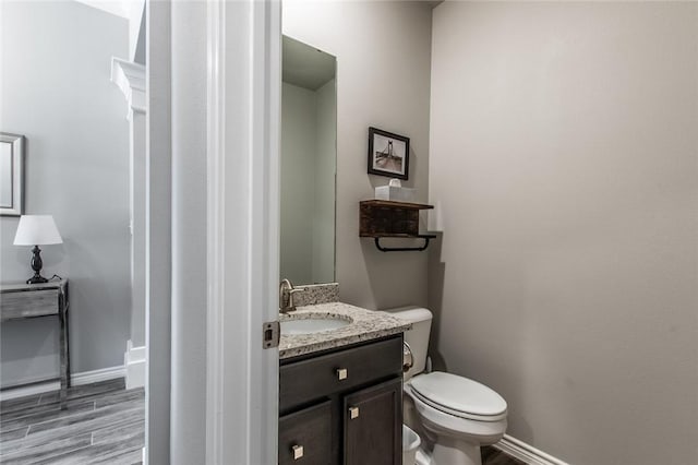 half bath with vanity, toilet, wood finished floors, and baseboards