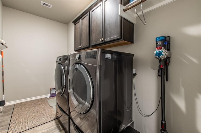 clothes washing area featuring visible vents, baseboards, washing machine and dryer, light wood-type flooring, and cabinet space