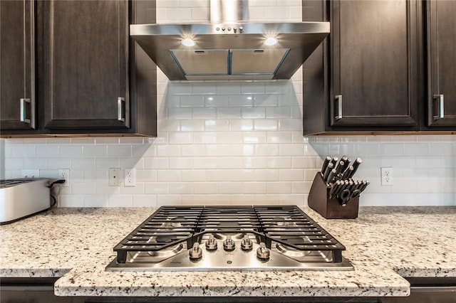 kitchen featuring dark brown cabinets, decorative backsplash, stainless steel gas stovetop, and wall chimney exhaust hood