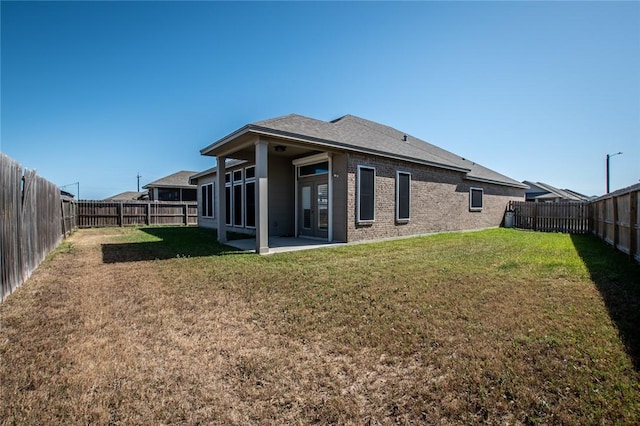 rear view of property featuring brick siding, a fenced backyard, a patio area, and a yard