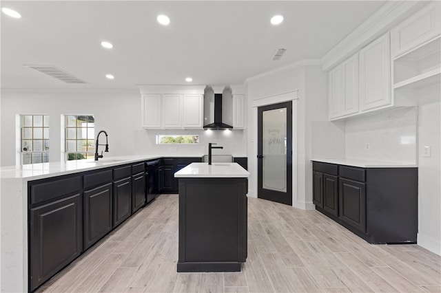 kitchen with kitchen peninsula, sink, wall chimney range hood, a kitchen island, and white cabinetry