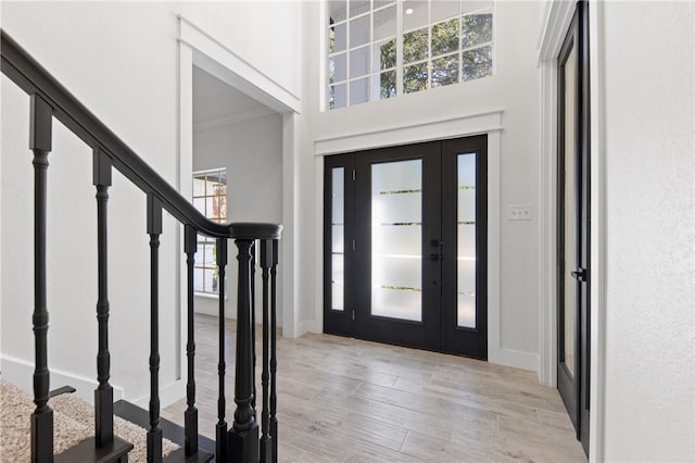 entryway featuring a high ceiling, crown molding, a healthy amount of sunlight, and light hardwood / wood-style flooring