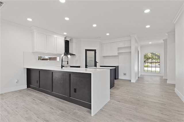 kitchen featuring white cabinetry, kitchen peninsula, wall chimney exhaust hood, and crown molding