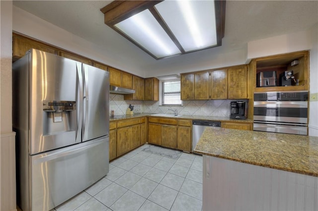 2413 Cricket Hollow St, Corpus Christi, TX 78414 - kitchen with appliances with stainless steel finishes, brown cabinetry, decorative backsplash, light tile patterned floors, and under cabinet range hood