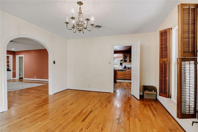 unfurnished dining area featuring an inviting chandelier, arched walkways, baseboards, and light wood finished floors