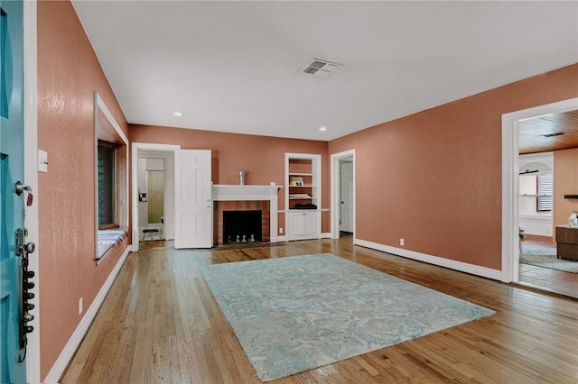 unfurnished living room with visible vents, built in shelves, wood finished floors, a tile fireplace, and baseboards