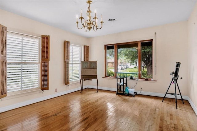 empty room with baseboards, a notable chandelier, visible vents, and hardwood / wood-style floors